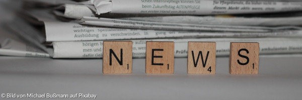 Scrabble-Steine mit dem Wort "News" vor einem Stapel Zeitungen
